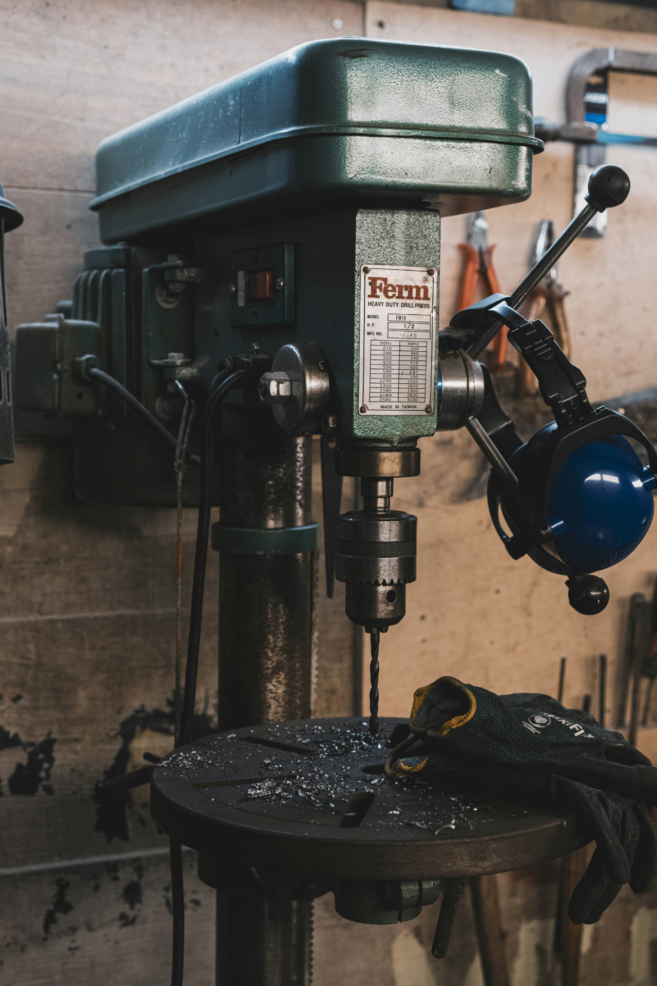 A green drill press with the bit pointed down at a workbench